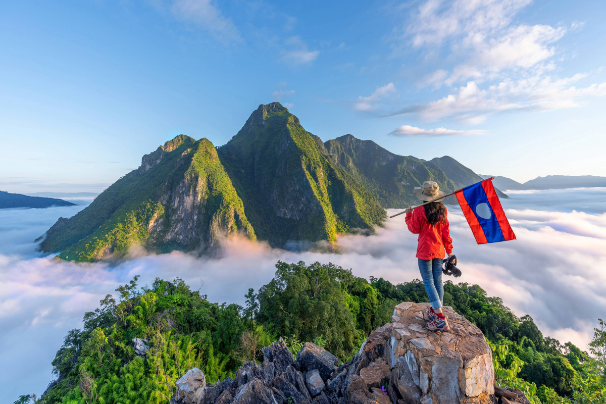 A woman holding the flag of Laos while standing on a mountain.