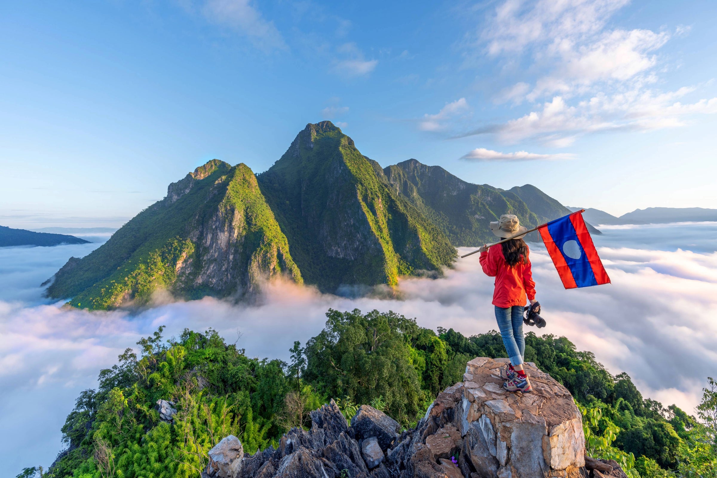 A woman holding the Laos flag on top of a mountain.