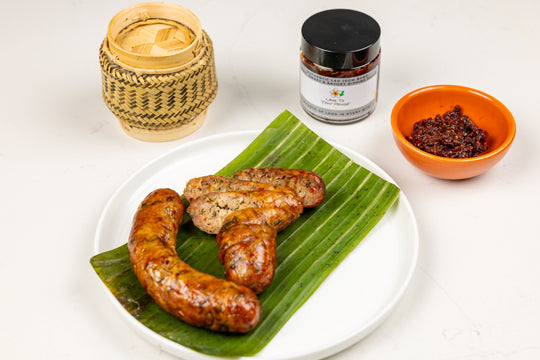 Grilled spicy sausage being displayed with a sticky rice basket, and jar of spicy dipping sauce.